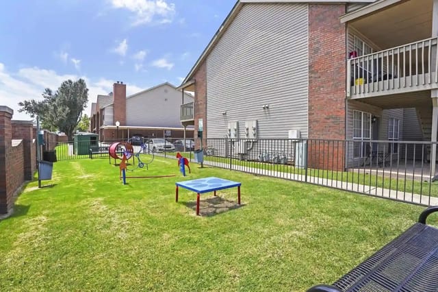 Grass courtyard with a children's playset, surrounded by apartment buildings and a metal fence.