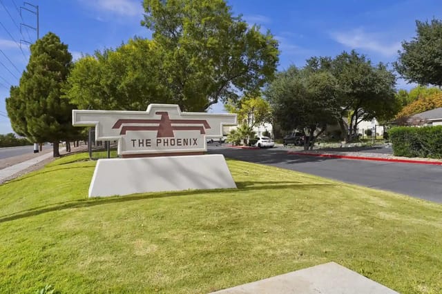 Entrance sign for The Phoenix apartment community with trees and a driveway