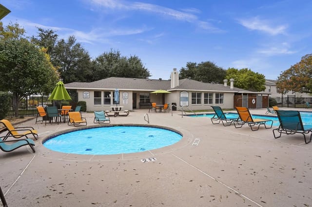 Two swimming pools and lounge chairs outside apartment building.