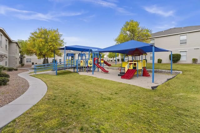 Playground with blue shade canopies and colorful equipment in a residential courtyard.