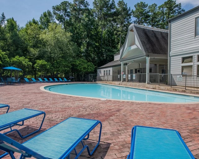 Outdoor community pool with blue lounge chairs on a brick deck beside a building.