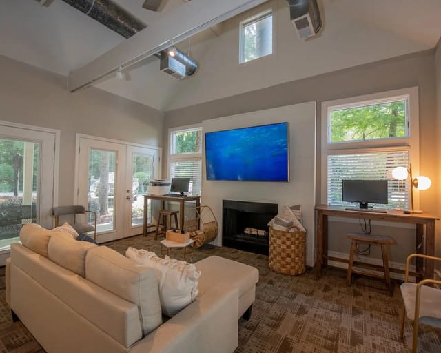 Interior common lounge with beige sofa, fireplace, large TV, and workstation desks.