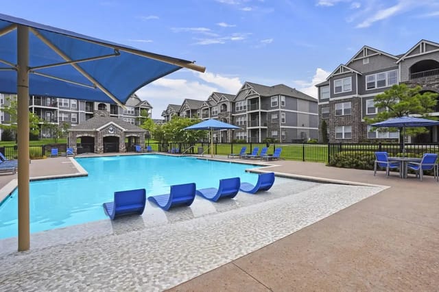 Outdoor communal pool area with blue lounge chairs and buildings in the background.