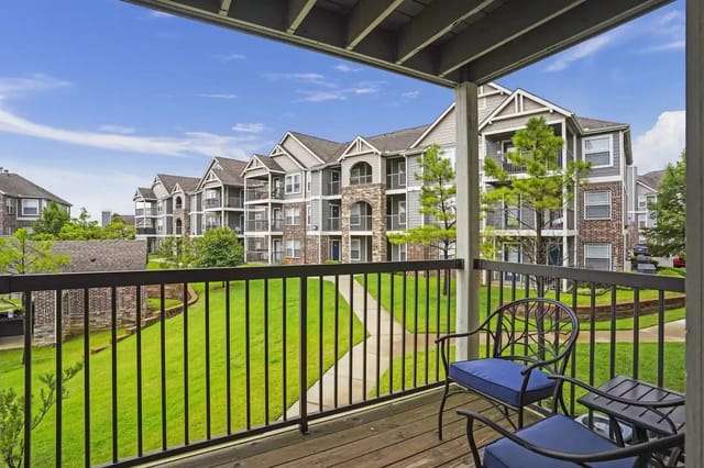 Balcony view of a modern apartment complex with green lawns and walking paths.