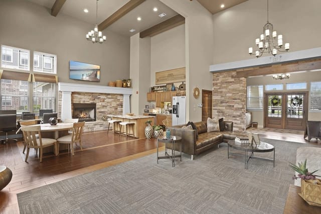Open community lounge with a fireplace, sofas, tables, and a kitchen area.