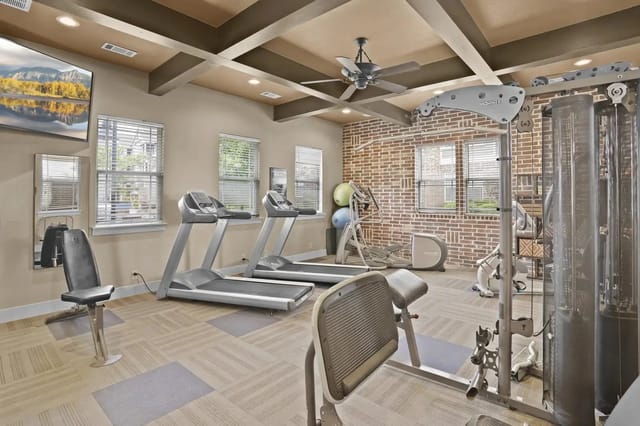 Fitness center with treadmills, weight machines, and brick accent wall.
