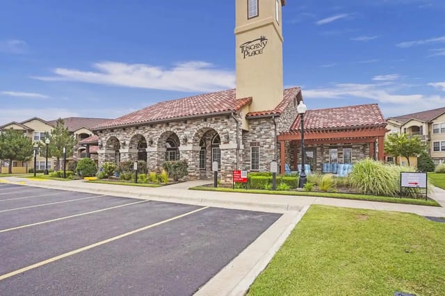 Exterior view of a stone community building with arched entrances and a tall Tuscany Place sign.