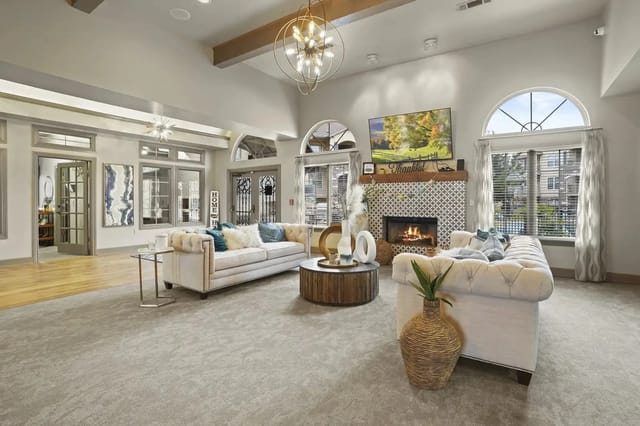 Interior community lounge with white tufted sofas, a stone fireplace, and a wall-mounted TV.