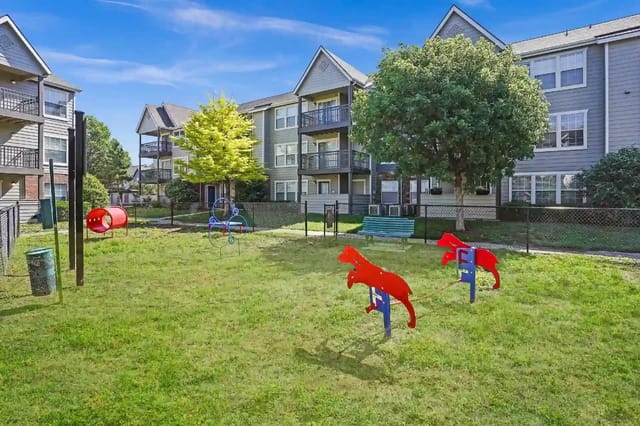 Outdoor playground in apartment community courtyard with grass, fence, and benches.