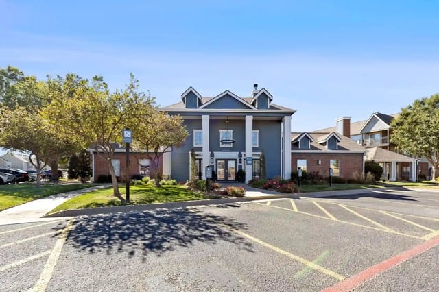 Exterior view of a blue-gray apartment community building with white columns and landscaping.