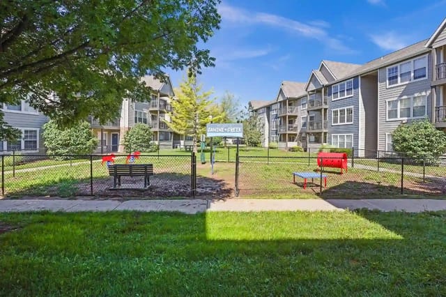 Fenced communal courtyard with a playground and benches between apartment buildings.