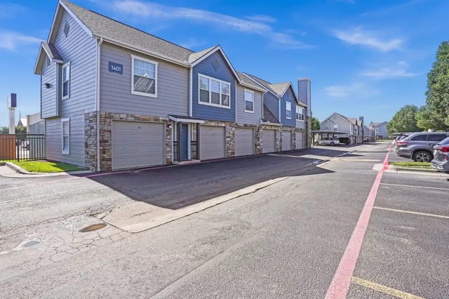 Exterior view of a row of townhome-style apartment buildings with attached garages along a paved street.