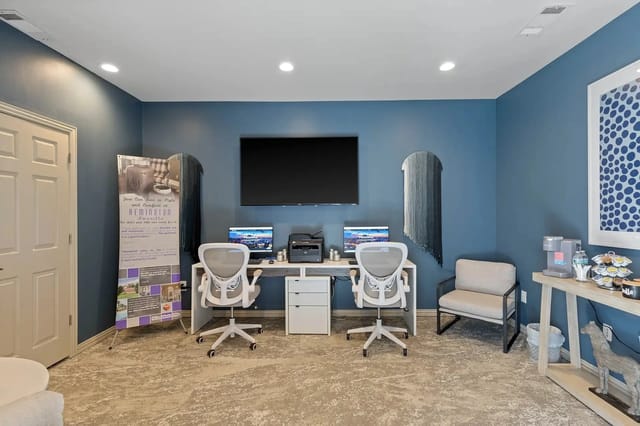 Blue-walled community workspace with two desks, computers, printer, and seating.