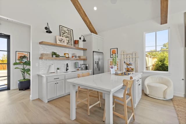 Bright modern kitchen with white cabinets, island, open shelves, and a large window.