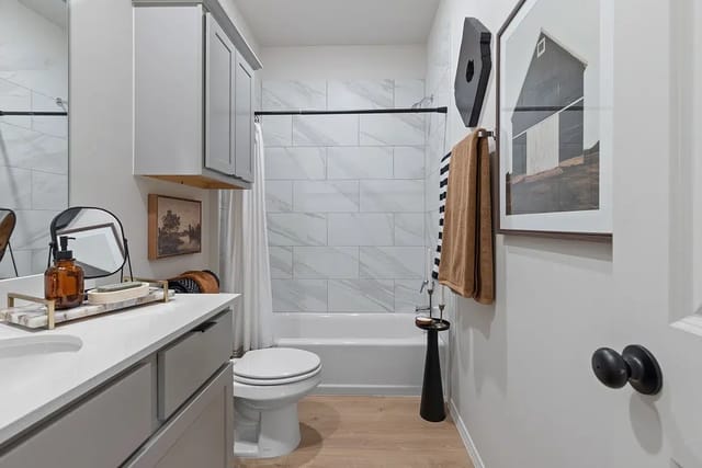 Modern gray bathroom with vanity, toilet, and tiled tub surround.