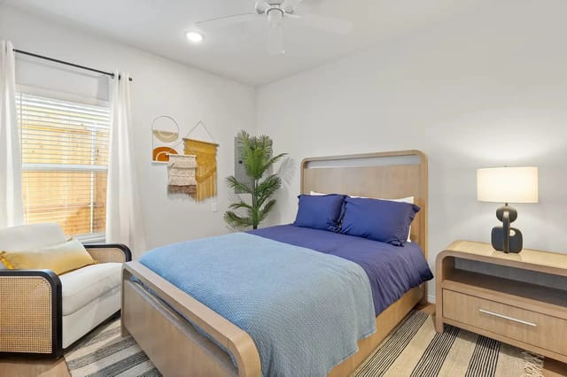 Bedroom in a modern apartment with a wooden bed, blue bedding, lamp, and plants.