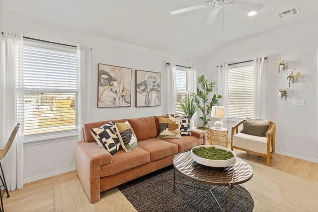 Bright living room featuring a peach sofa, a round metal coffee table, and green plants.