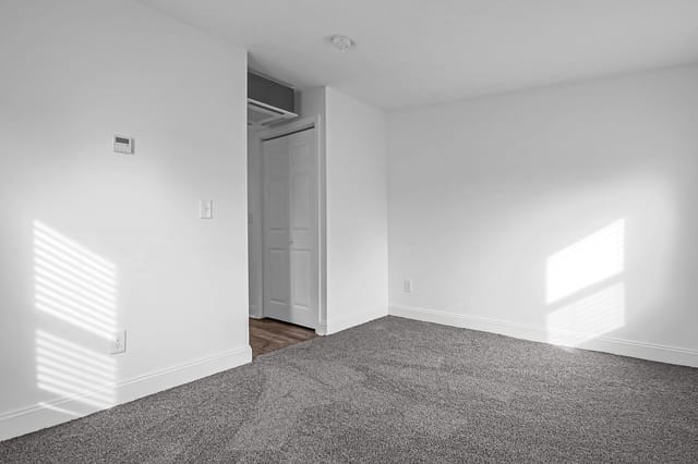 Empty apartment bedroom with gray carpet and white walls.