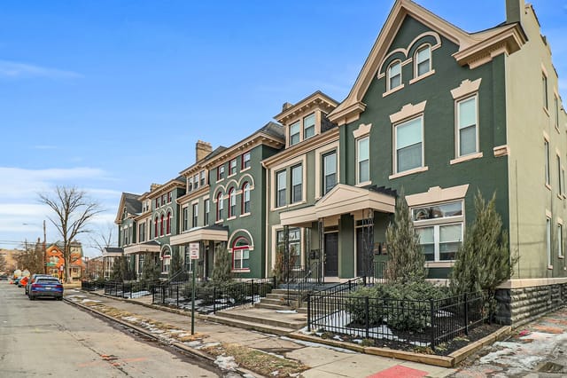 Exterior view of historic green apartment buildings with decorative trim and arched windows.