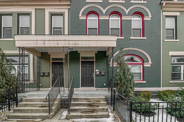 Exterior of a historic apartment building with green brick facade and arched windows.