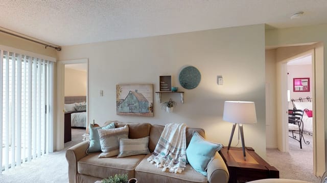 Cozy living room with a beige sofa, decorative pillows, a throw blanket, and a barn-themed painting on the wall.