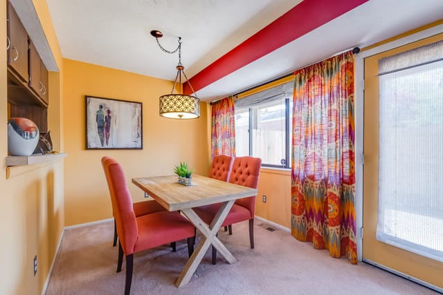 Dining room with a wooden table, four orange chairs, and colorful curtains.