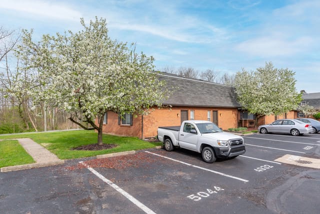 Exterior of brick apartment buildings with blooming trees and parked cars.