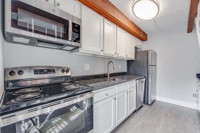 Stainless steel stove, microwave, refrigerator, sink, and dishwasher in a small kitchen with white cabinets.