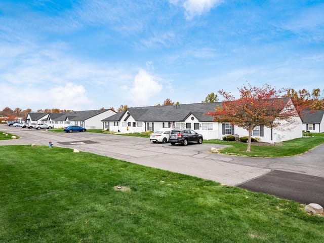 Exterior view of apartment buildings with manicured lawns and parked cars.