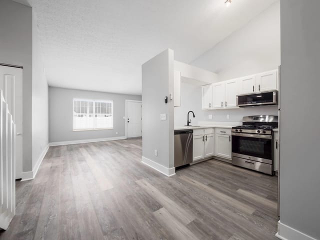 Modern kitchen with white cabinets and stainless steel appliances, connected to a living area with a large window.
