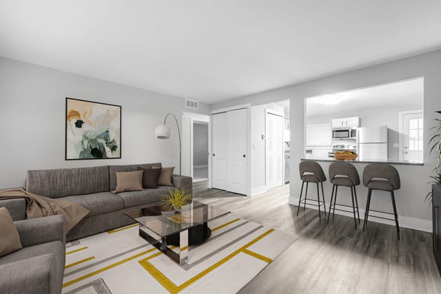 Living room with a sofa, coffee table, and a view into the kitchen with bar stools.
