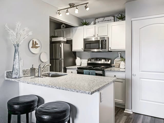Modern kitchen with granite countertops, stainless steel appliances, and a breakfast bar with stools.