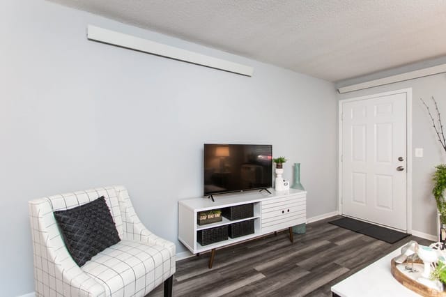 A modern living room with a plaid armchair, a white media console with a TV, and a white front door.