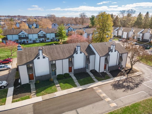 Townhouses with white exteriors and dark trim, set against a backdrop of trees and a bright blue sky.