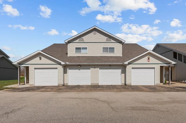 Exterior view of a building with four garage doors and a cloudy blue sky.