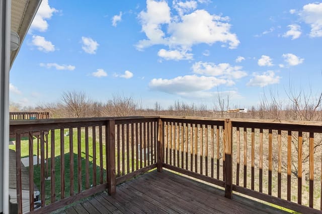 Wooden deck overlooking a grassy area and trees under a cloudy blue sky.