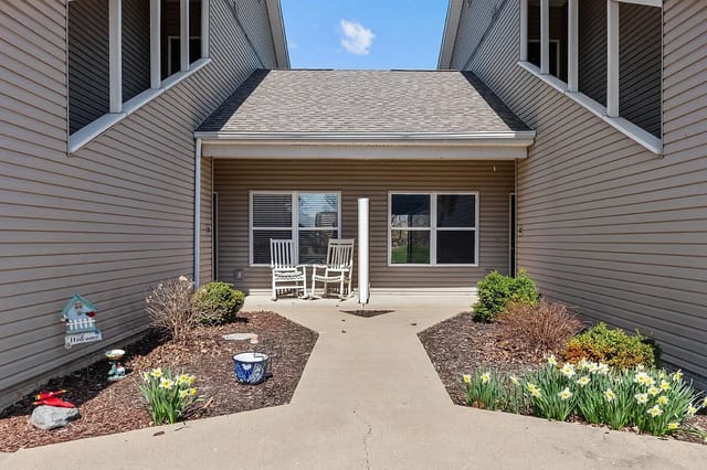 Apartment building exterior with a walkway leading to two doors, flanked by rocking chairs and blooming daffodils.