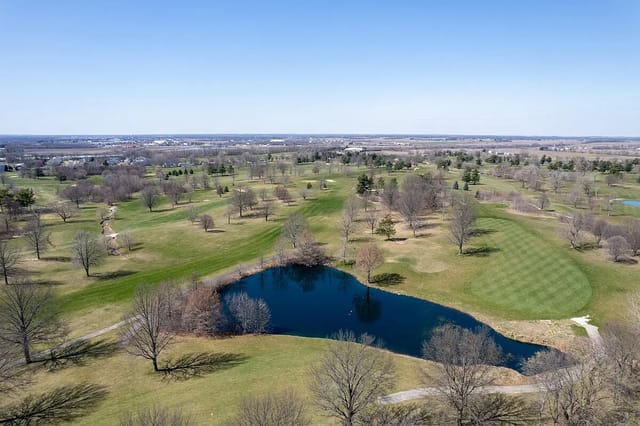 Aerial view of a golf course with a pond and distant cityscape.