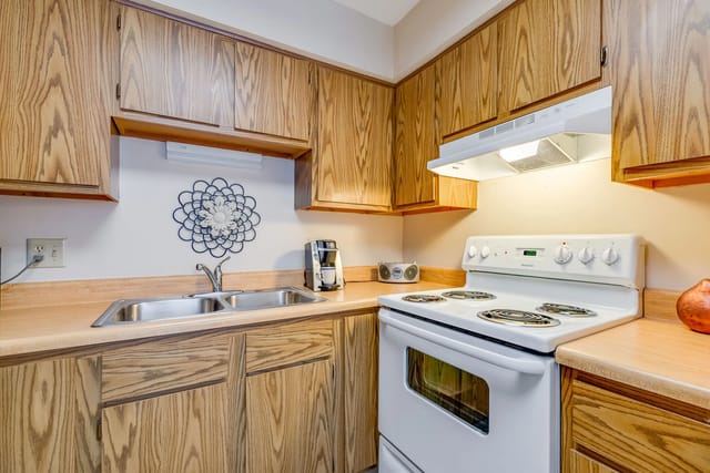 Kitchen with light wood cabinets, double sink, and white stove.