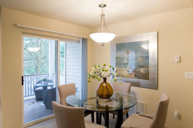 Dining area with glass table, chairs, and artwork, leading to a balcony.