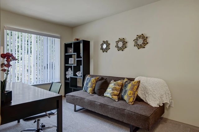 Desk and sofa in a well-lit room with vertical blinds and decorative wall art.
