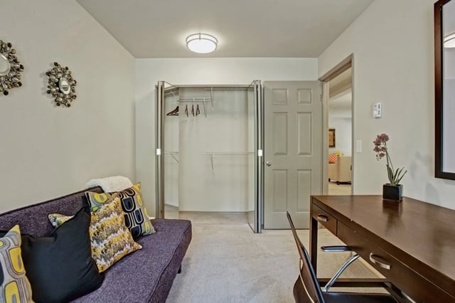 A furnished studio apartment with a sofa, desk, and closet.