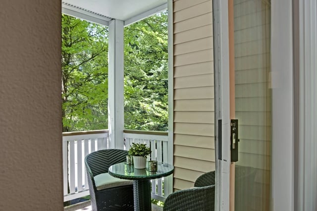 Balcony with wicker furniture and a small table overlooking lush green trees.