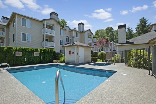 Swimming pool and hot tub area at apartment complex with beige buildings in the background.