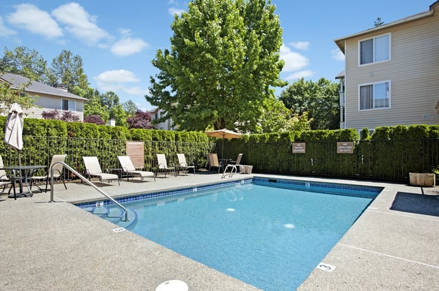 Outdoor swimming pool area with lounge chairs and umbrellas, surrounded by lush greenery and apartment buildings.