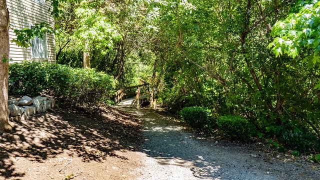 Gravel path leading to a wooden bridge through a lush, green, wooded area.