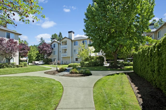 Apartment buildings with manicured lawns and walking paths under a blue sky.