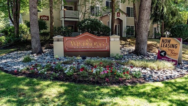 Wind Song Apartments monument sign with landscaping and a 'Now Leasing' sign.
