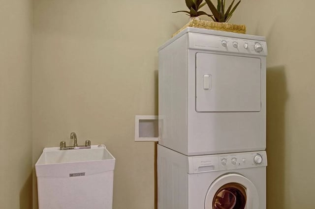 Stacked white washer and dryer with a utility sink.