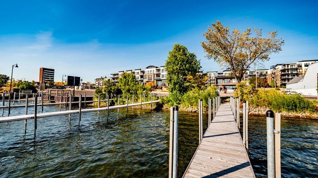 Wooden dock leading to apartment buildings by a lake.